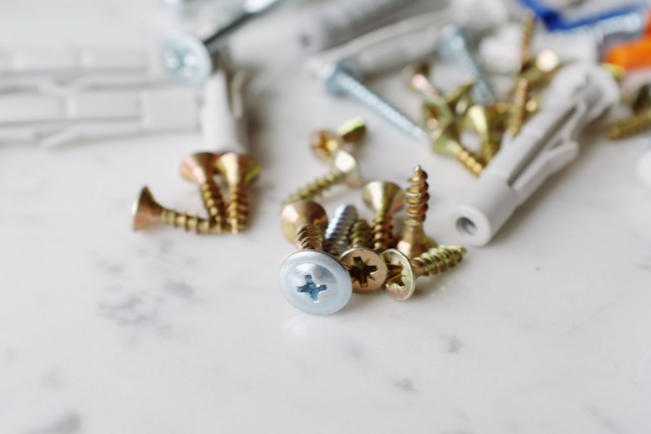 Set of various plastic dowels with assorted metal screws of different sizes placed on white marble table in modern workshop
