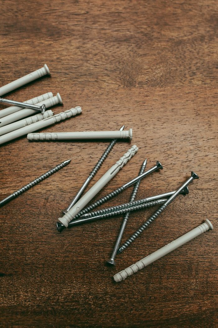 Assorted screws and plugs scattered on a textured wooden surface, perfect for DIY or construction themes.